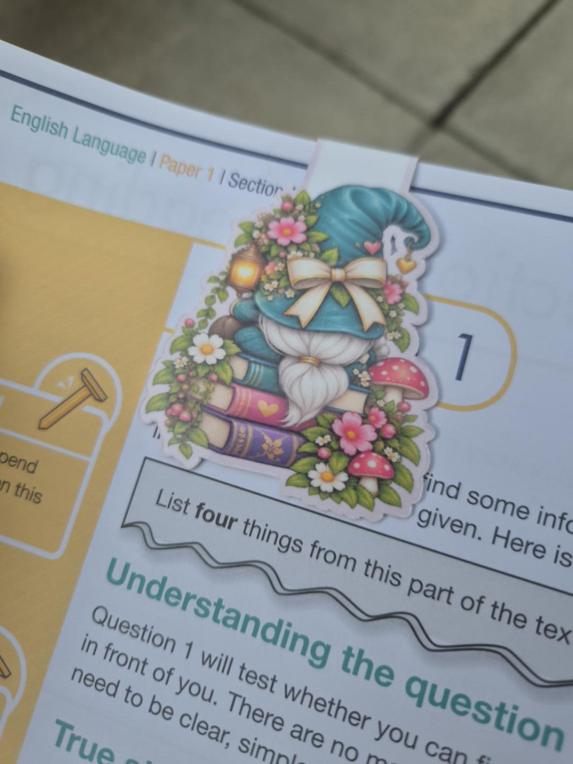 Back of reading gnome magnetic bookmark with teal hat, flowers, mushrooms and books